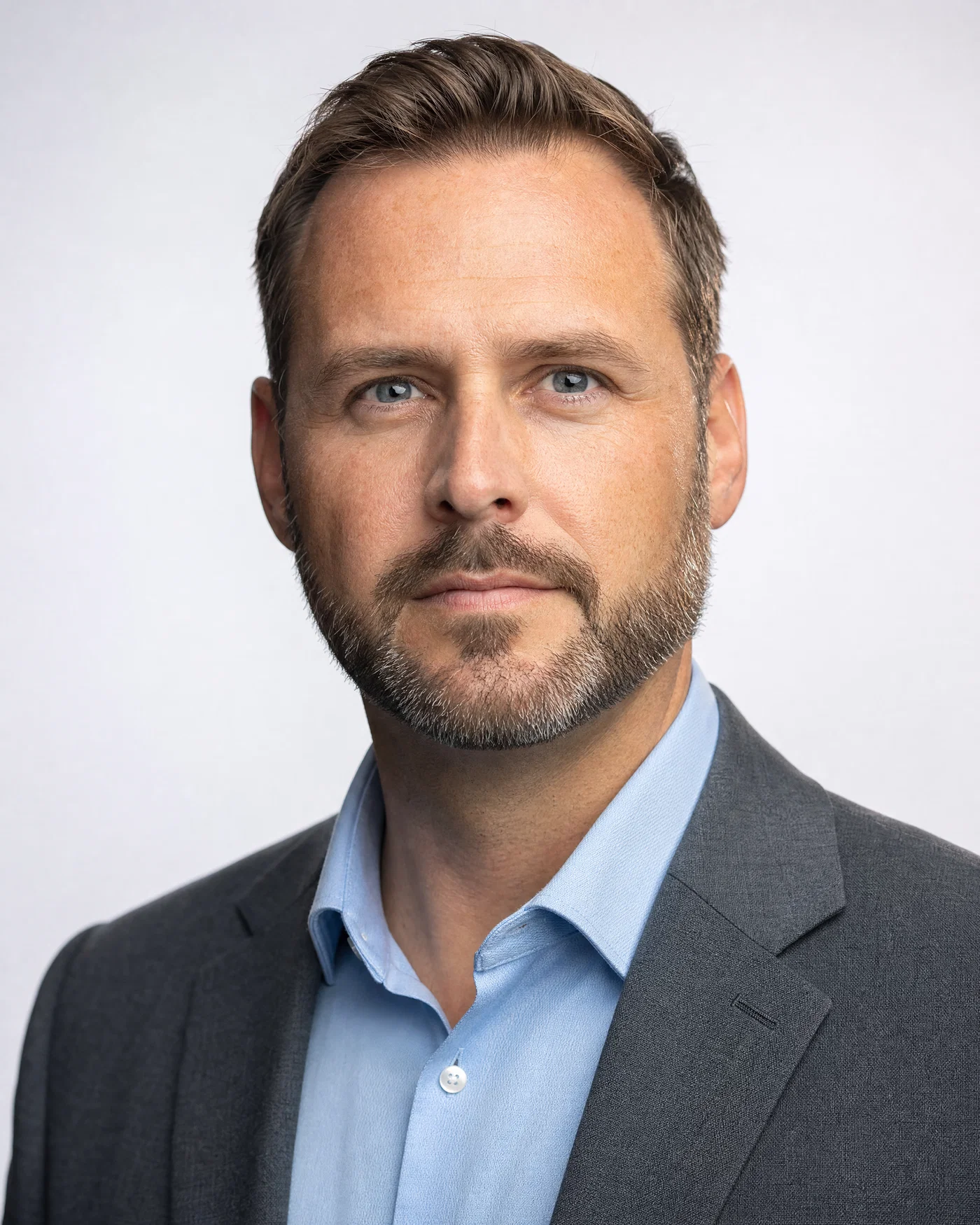 Bearded man in gray blazer on cool-white seamless with crisp rim along jawline.