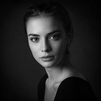 Black-and-white studio portrait with Rembrandt lighting and film grain, focused on eyes.