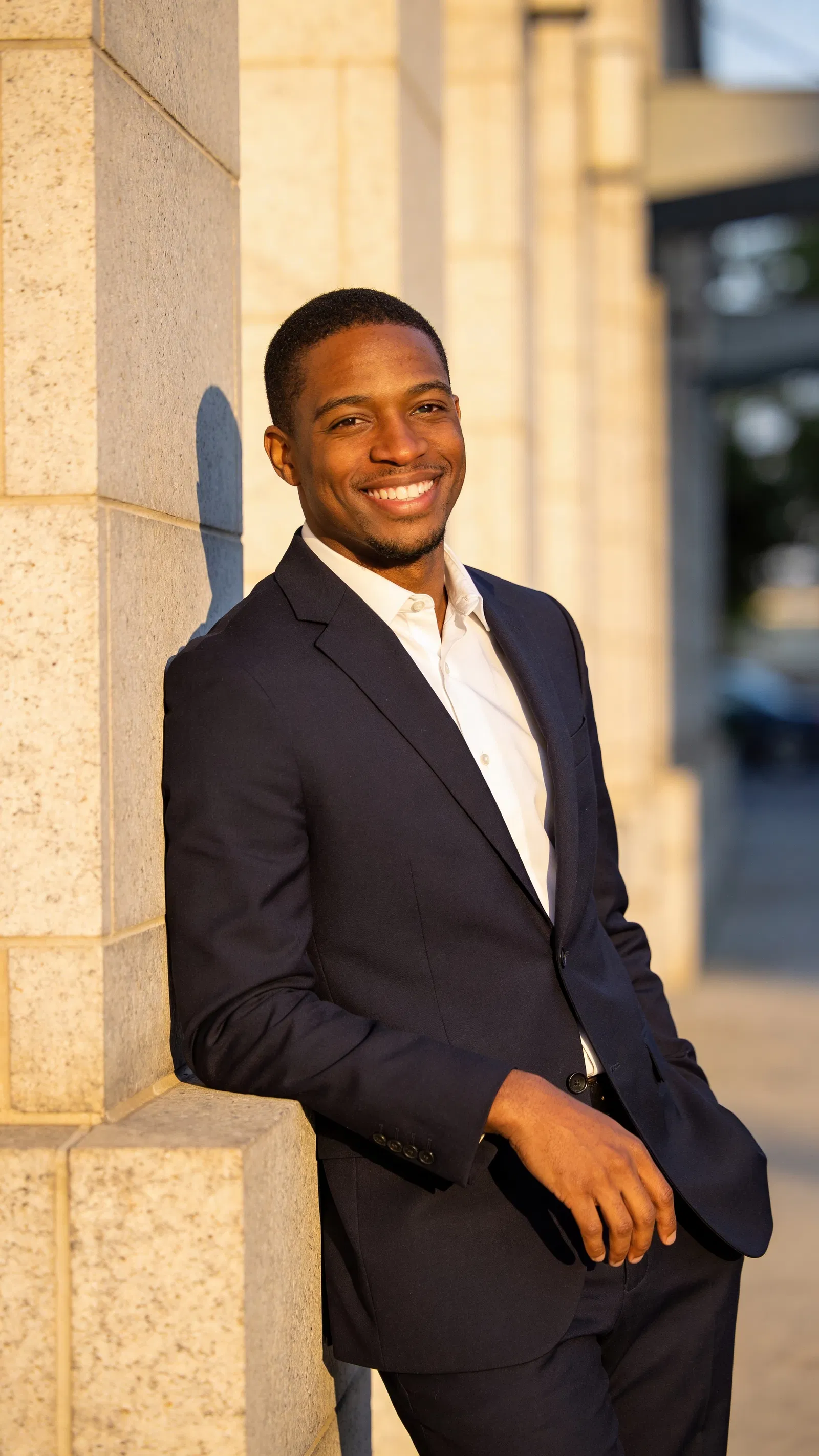 Black male attorney outdoor lifestyle headshot leaning on stone wall, confident smile