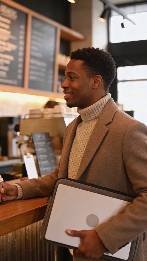 Black man at café counter holding laptop sleeve, professional approachable portrait