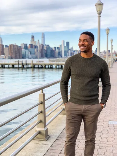 Black man by waterfront promenade, confident smile, modern dating profile portrait.
