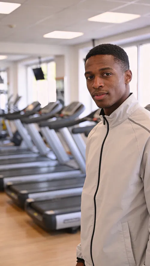 Black man in gym lobby wearing athletic jacket, confident profile portrait