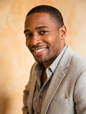 Black man in light-gray blazer against neutral wall for resume photo