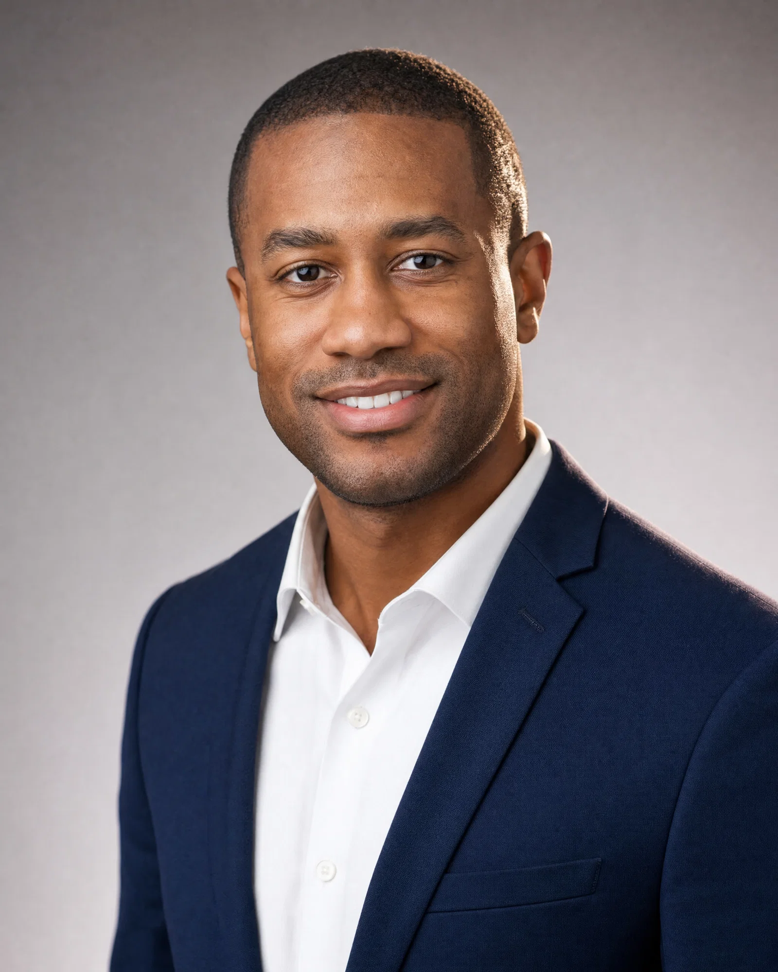 Black man in navy blazer on neutral gray seamless, soft key and rim light.