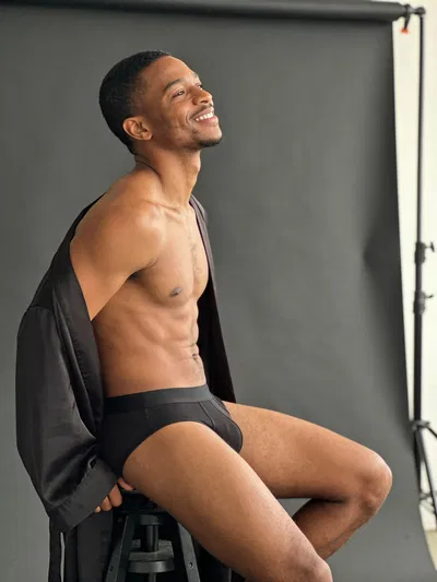 Black man in studio male boudoir portrait, seated confidently with softbox lighting