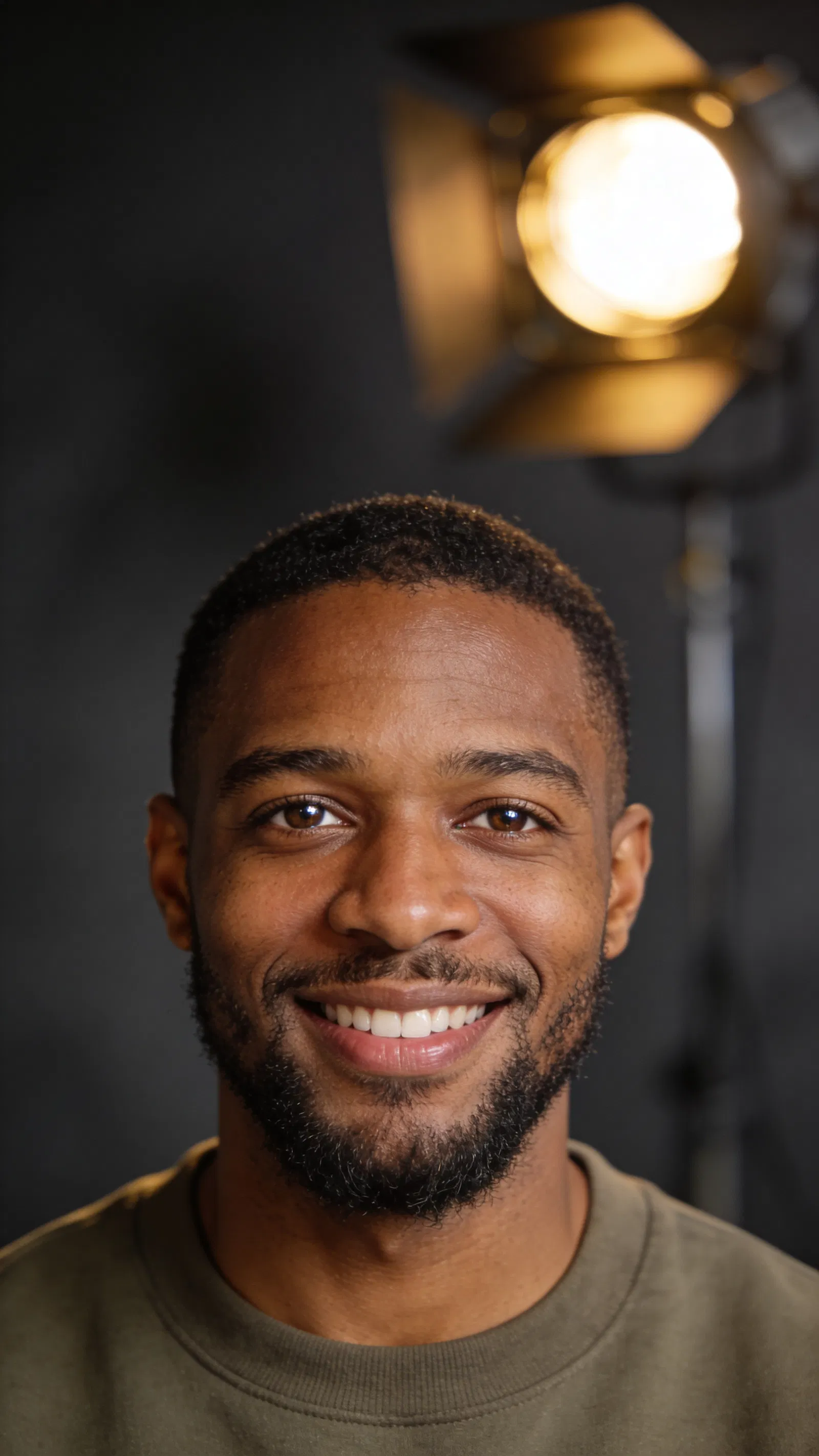 Black man studio headshot on charcoal background, confident smile for dating app.