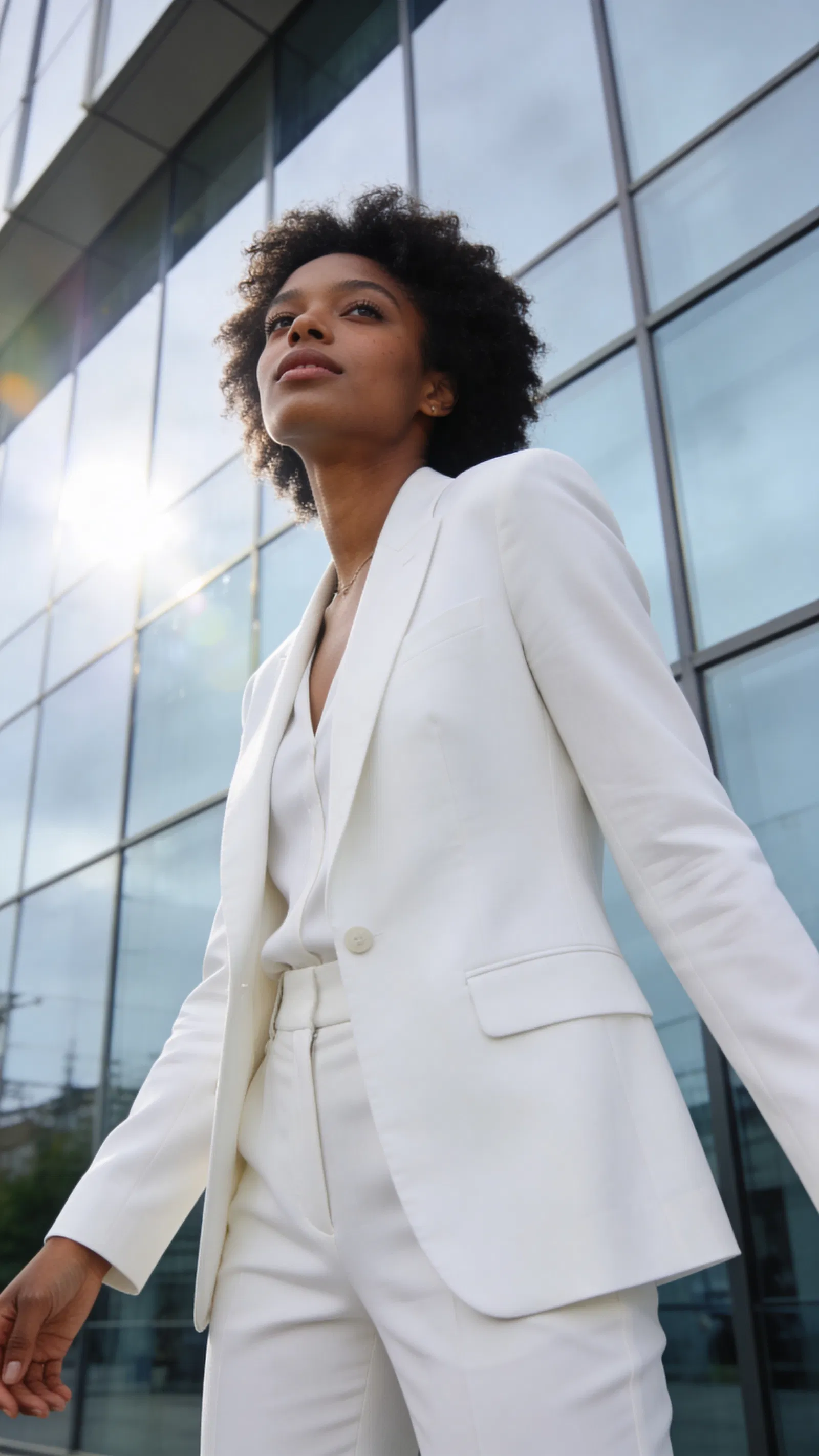 Black woman in white blazer outdoors by glass building with clean editorial lighting