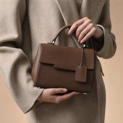 Close-up hands holding structured handbag with crisp leather grain under controlled studio light.