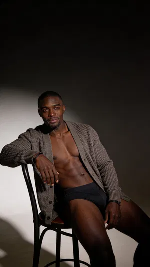 Consistent character in moody studio male boudoir scene with rim lighting and cardigan