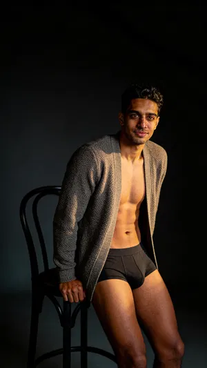 Consistent character in moody studio male boudoir scene with rim lighting and cardigan