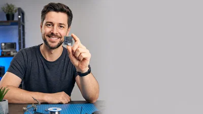 Creator at a clean tech desk holding a circuit board, with empty gray panel space for headline text