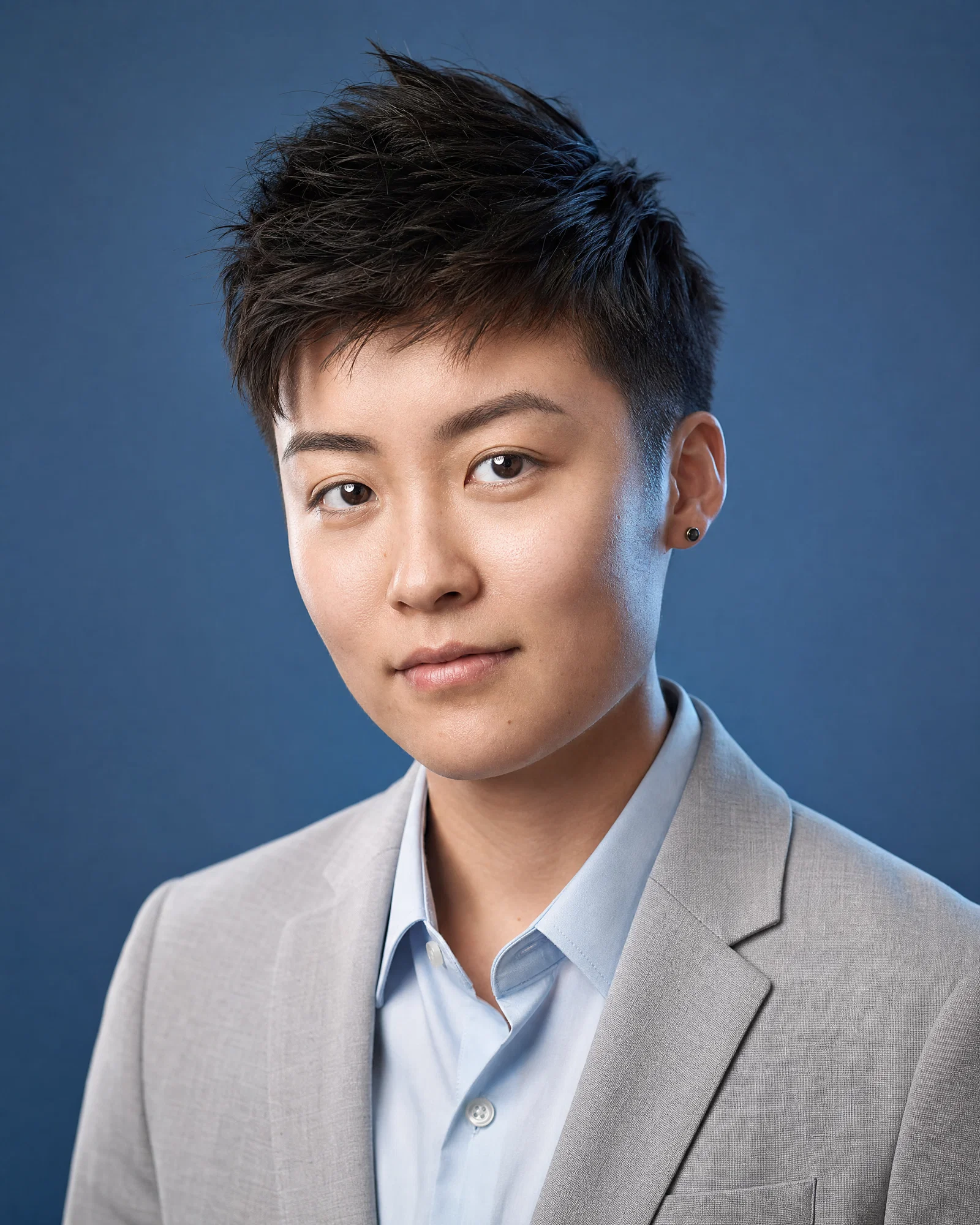 East Asian professional on slate-blue seamless with soft key and rim light separation.