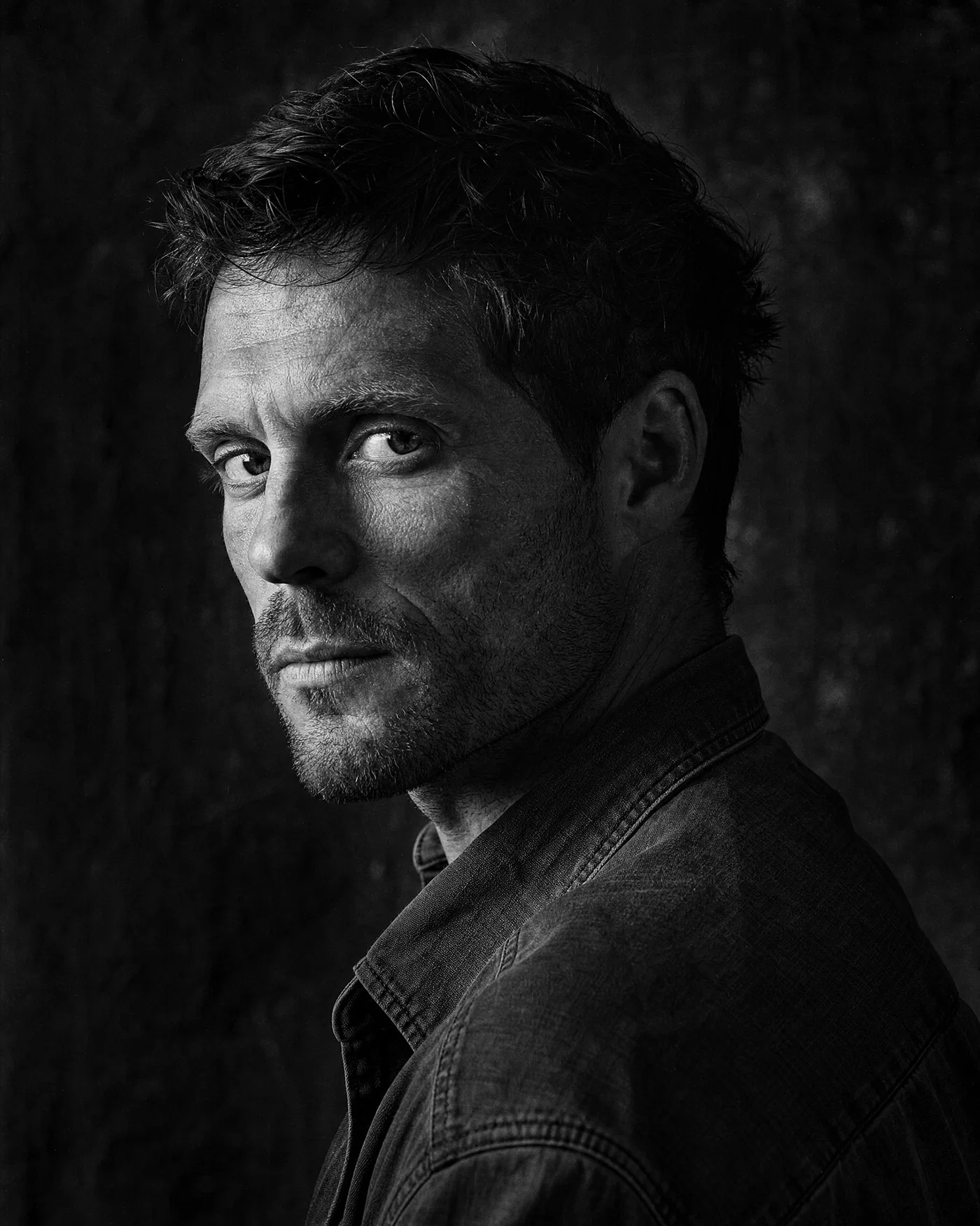 High-contrast black-and-white portrait with hard side light and visible grain.
