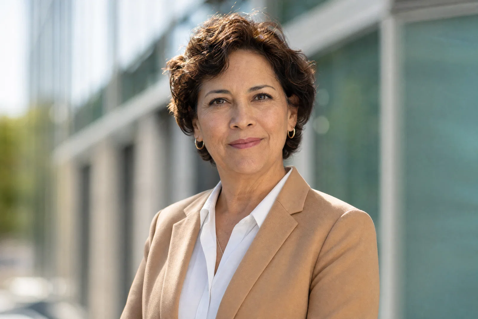 Latina executive headshot outdoors with office building bokeh, soft key and rim sunlight.