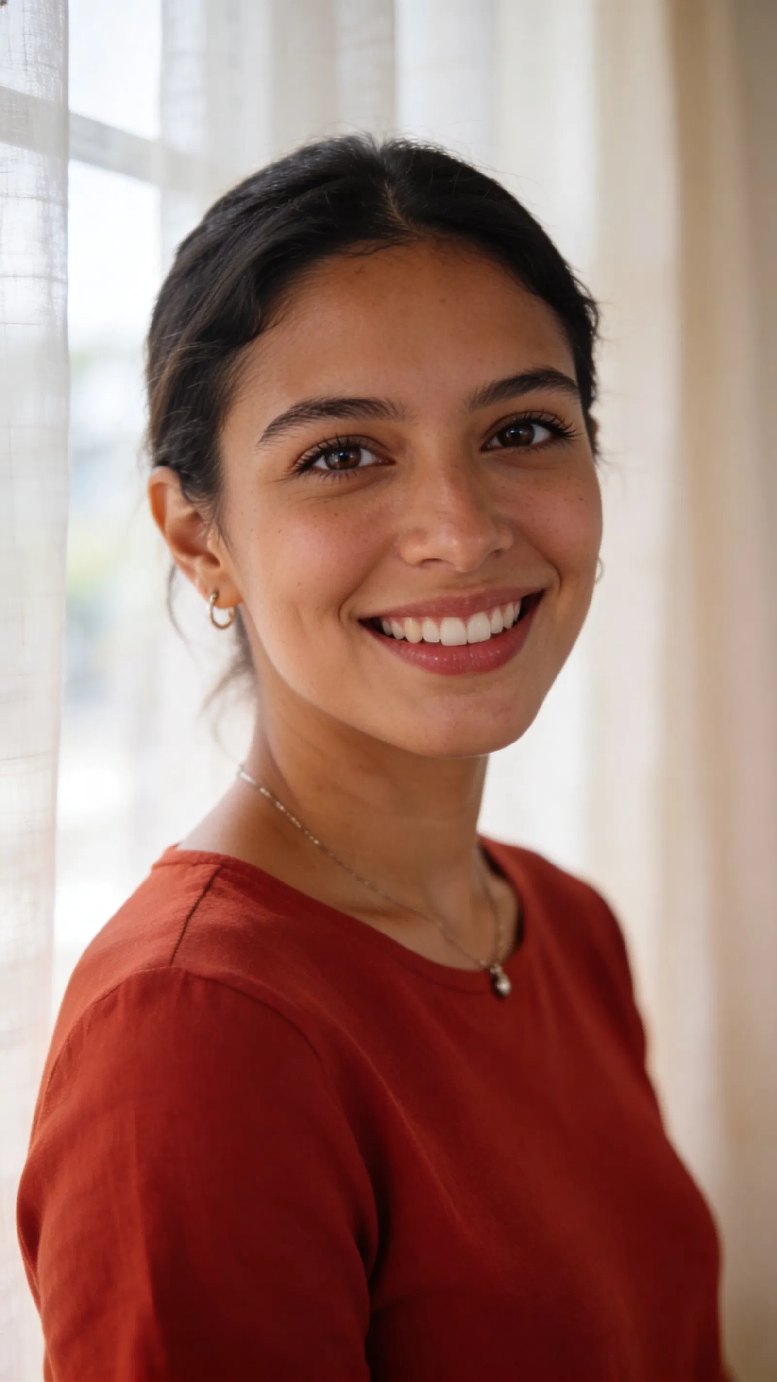 Latina woman in window light, natural head-and-shoulders dating profile photo.