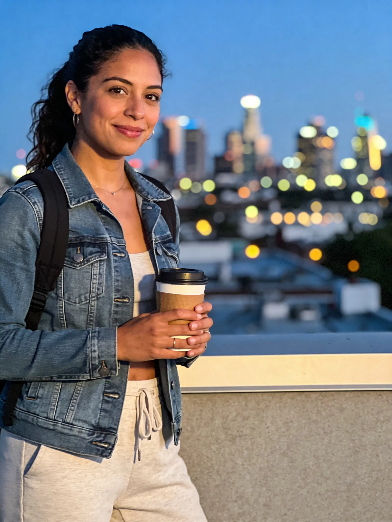 Latina woman on rooftop at dusk, city skyline travel lifestyle portrait.