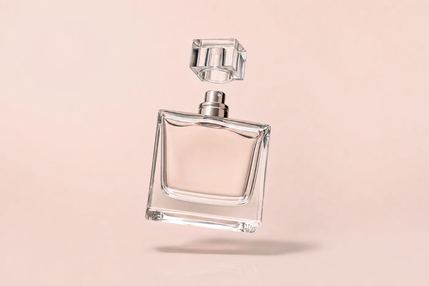 Levitating clear perfume bottle on blush seamless with soft overhead light and believable shadow.