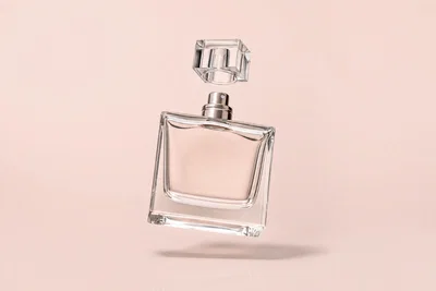 Levitating clear perfume bottle on blush seamless with soft overhead light and believable shadow.