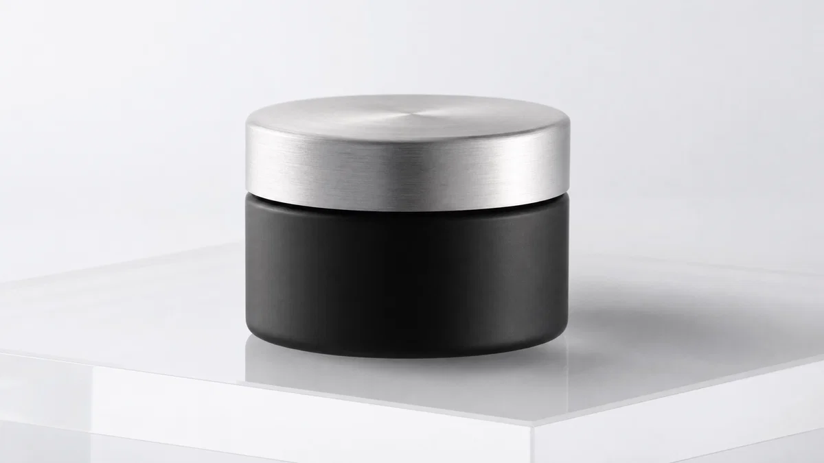 Matte black skincare jar on white seamless, softbox lighting and subtle reflection.