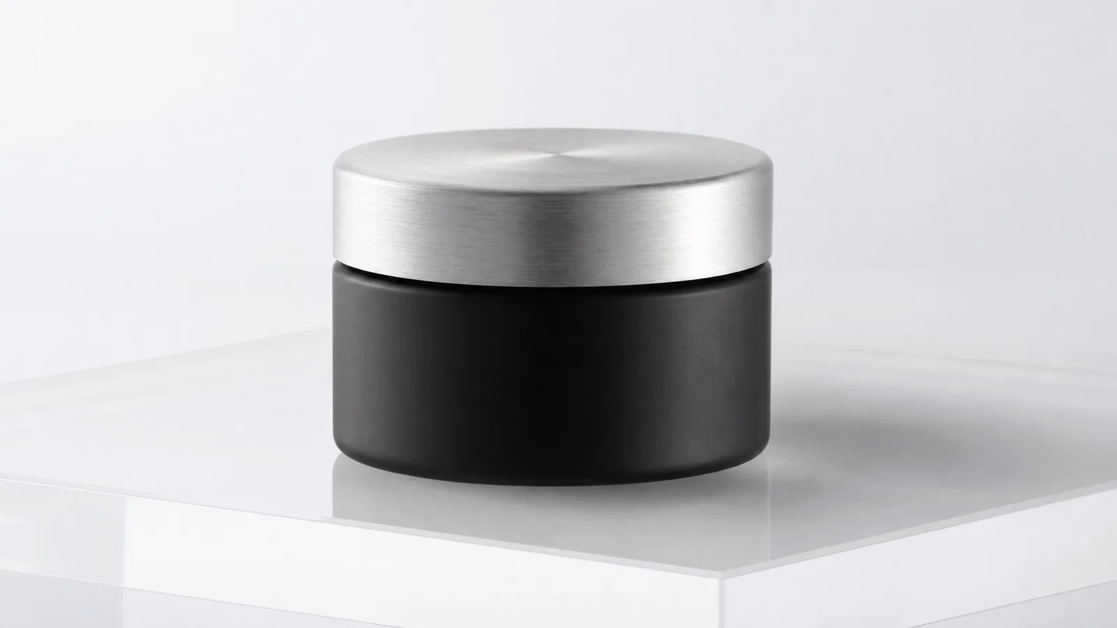 Matte black skincare jar on white seamless, softbox lighting and subtle reflection.