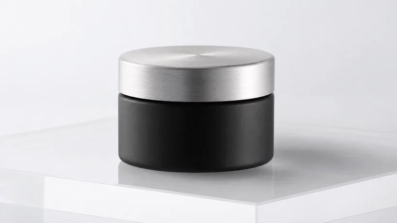 Matte black skincare jar on white seamless, softbox lighting and subtle reflection.