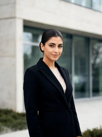 Middle Eastern woman outdoors in tailored coat, poised confident looksmaxxing portrait