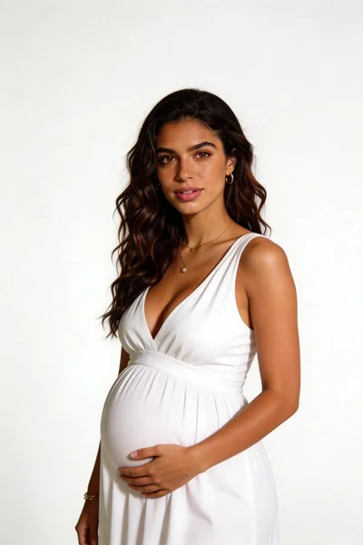 Olive-skinned pregnant woman in studio wearing white maternity dress