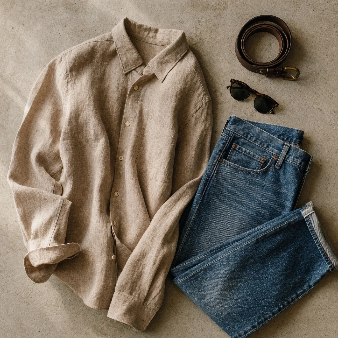 Overhead outfit flat-lay on concrete with soft directional light revealing fabric texture.