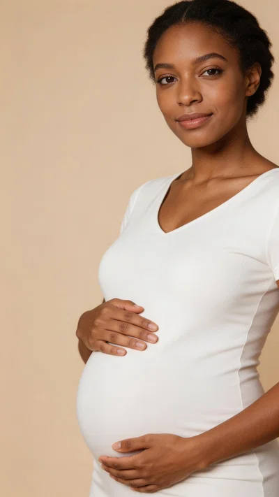Pregnant Black woman in white maternity dress on beige studio backdrop