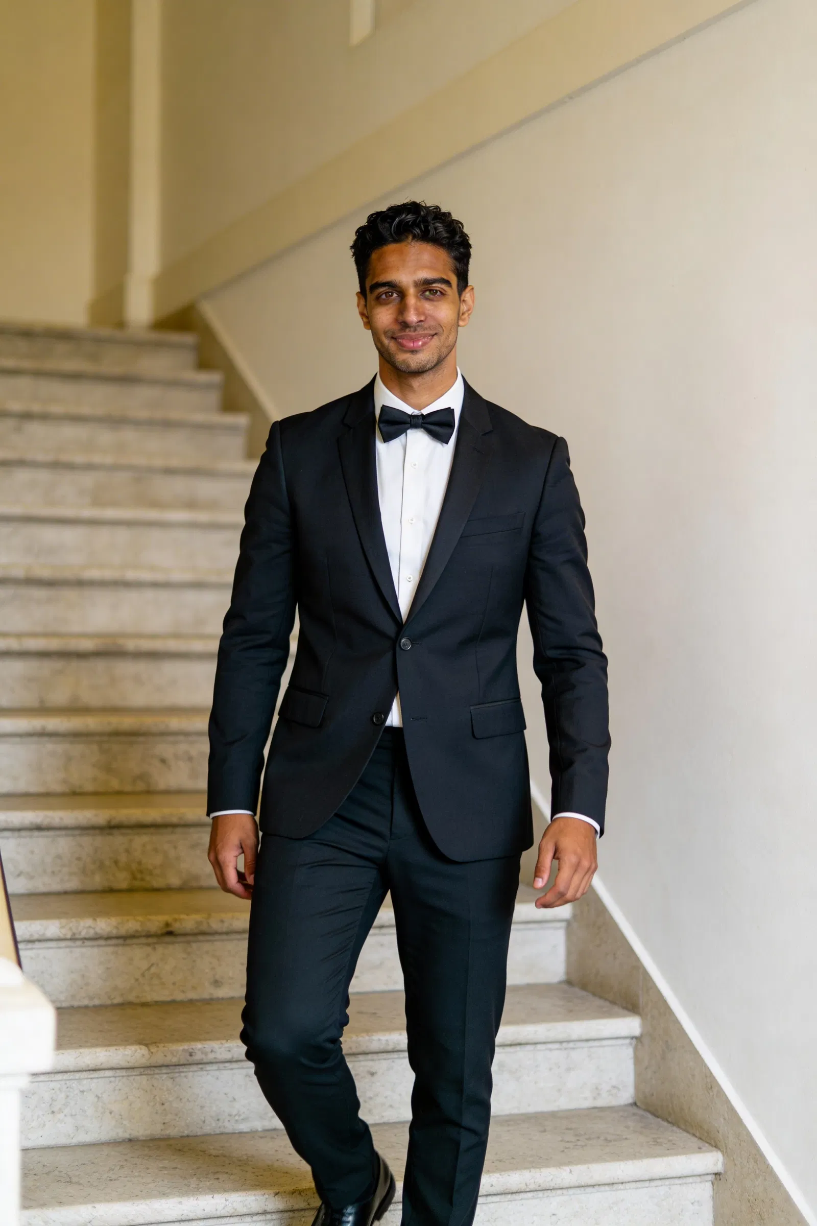Same groom character walking on venue staircase in tux 2:3