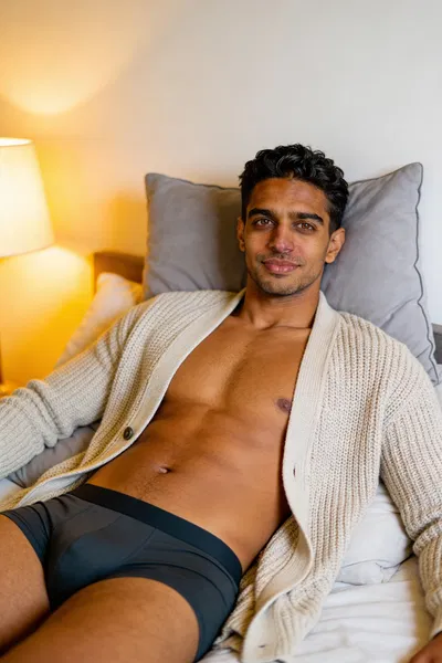 Same man reclining on bed in warm lamp-lit dudeoir photo