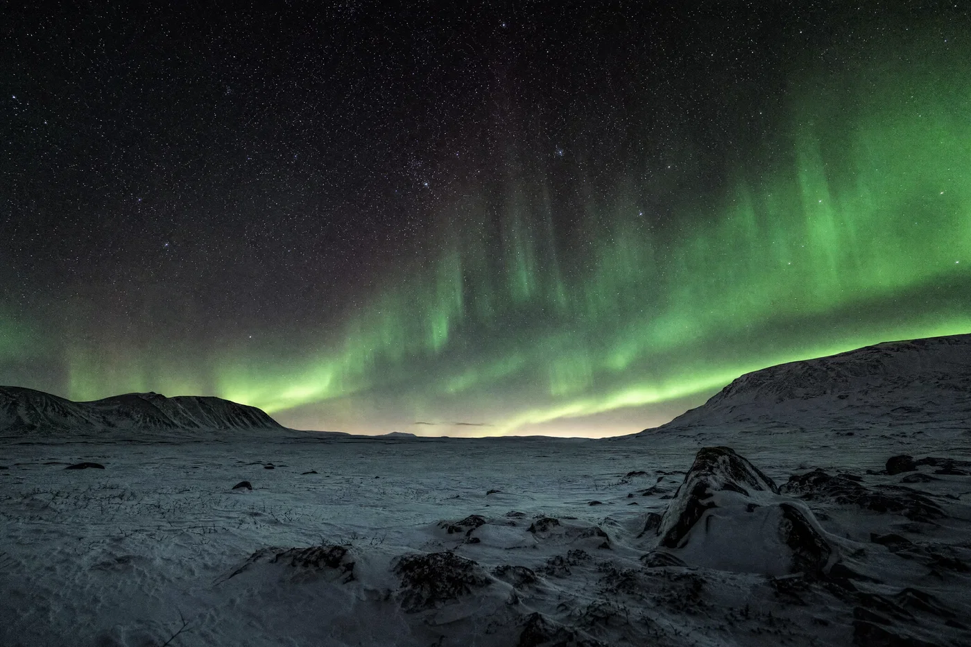 Snowy tundra under green aurora and sharp stars with neutral whites and deep blacks.