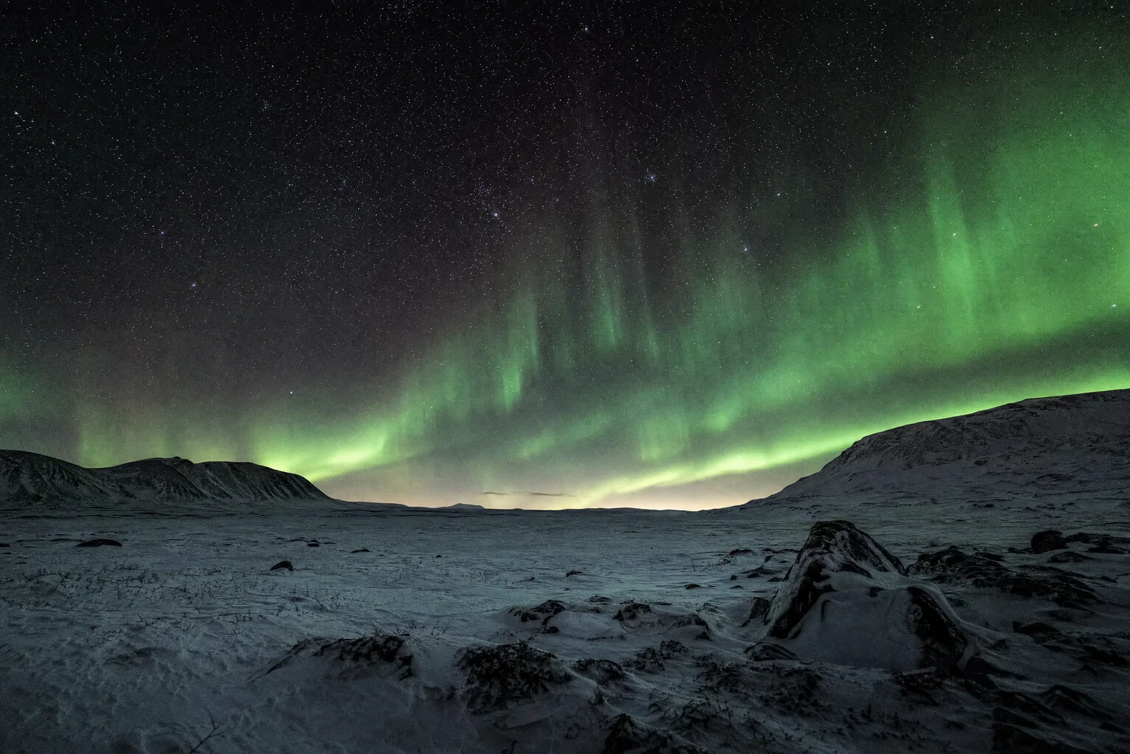 Snowy tundra under green aurora and sharp stars with neutral whites and deep blacks.