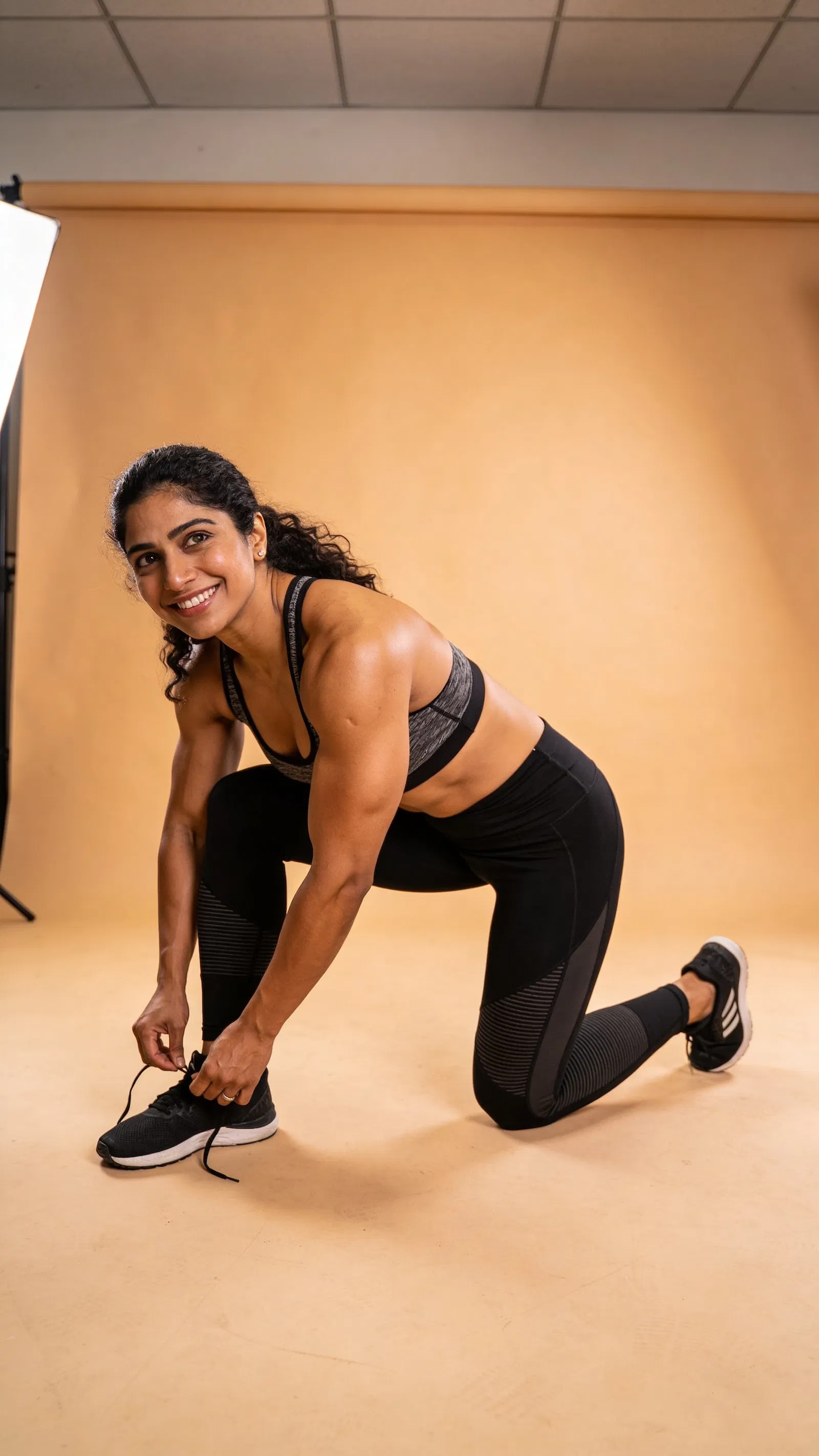 South Asian female bodybuilder studio portrait tying shoe, friendly expression