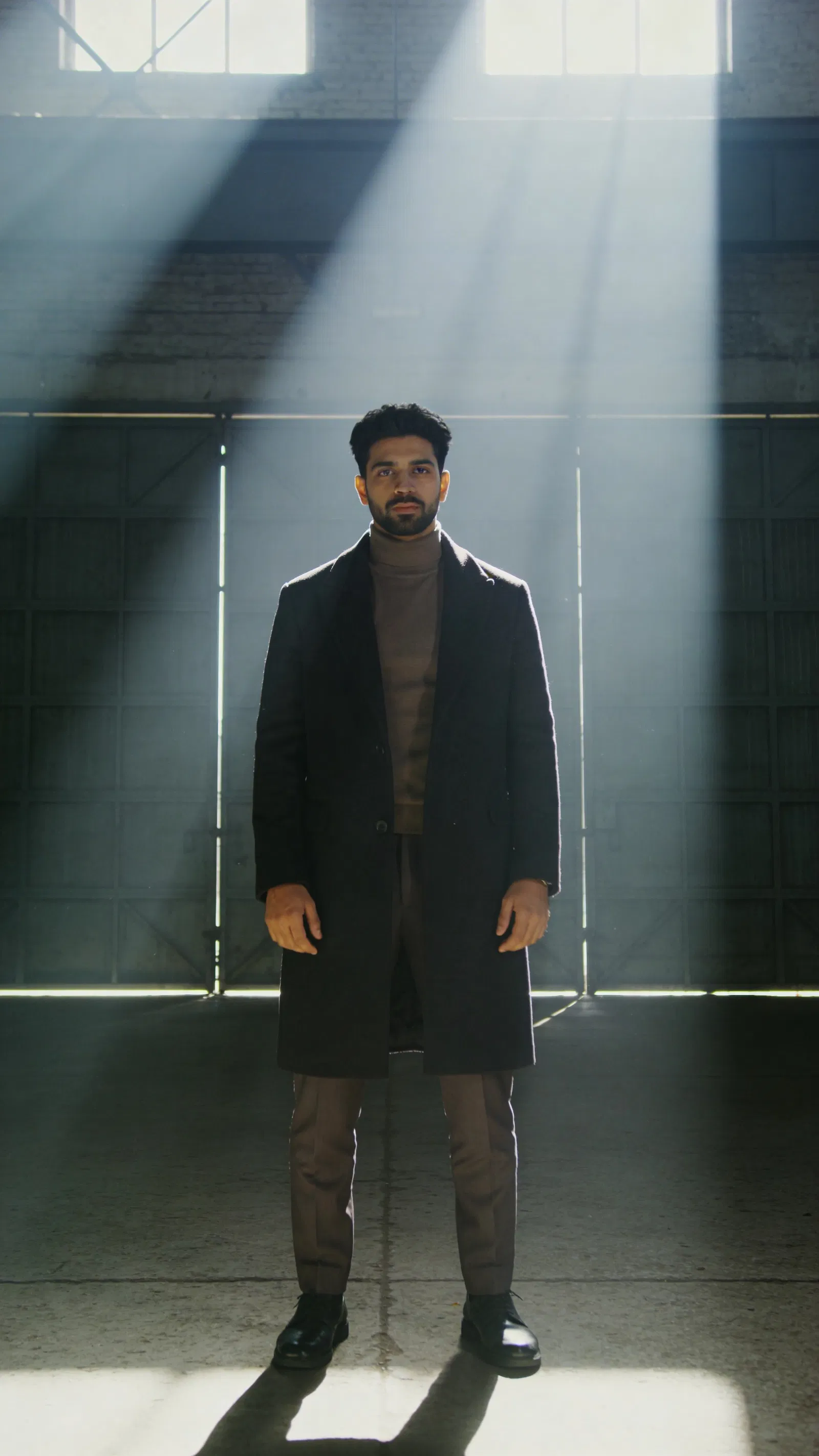 South Asian man full-body warehouse editorial portrait with dramatic light beams
