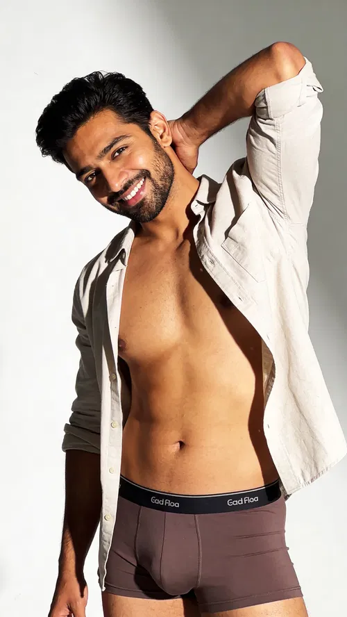 South Asian man in bright studio with relaxed hand-behind-neck pose for playful male boudoir portrait