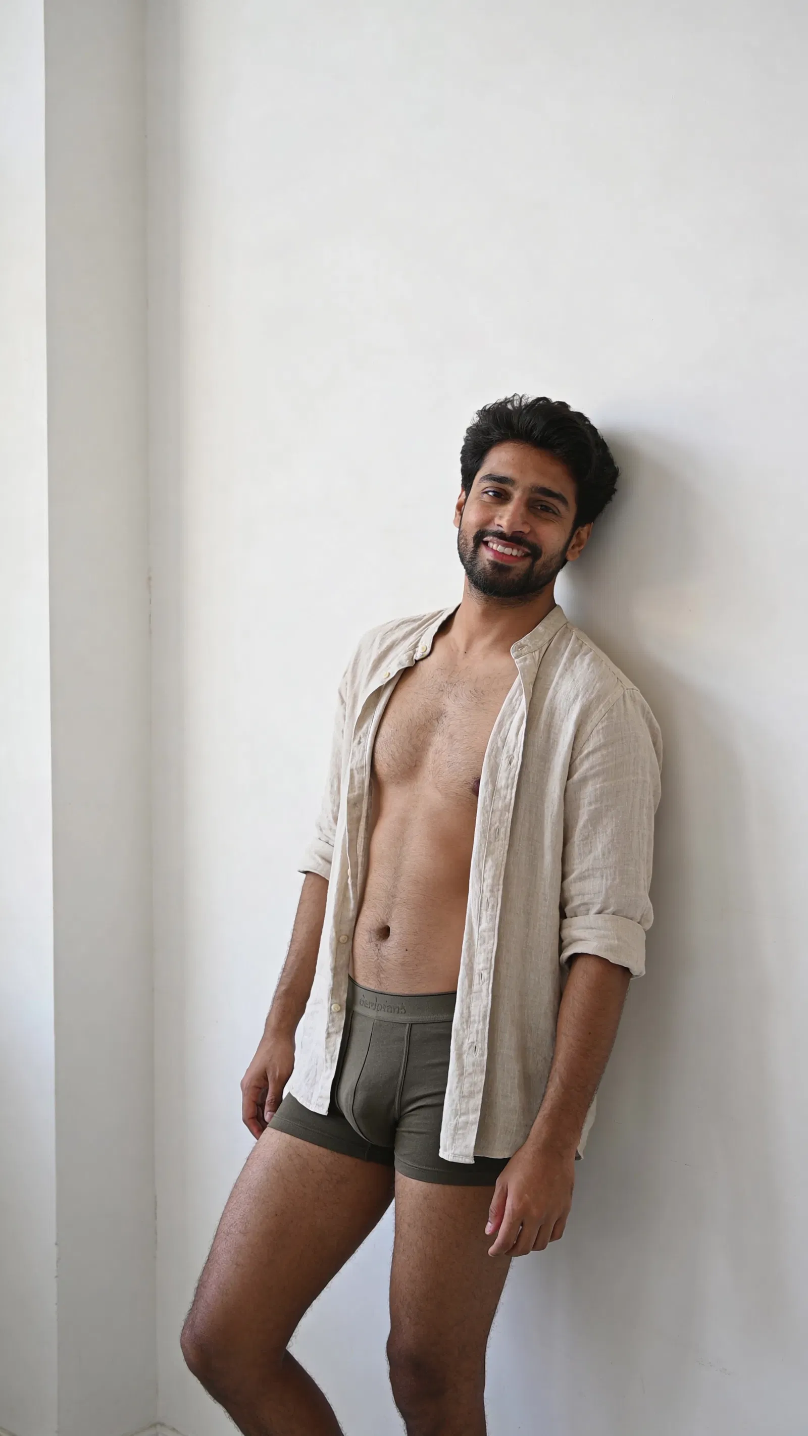 South Asian man standing against white wall in minimalist tasteful boudoir photo for men