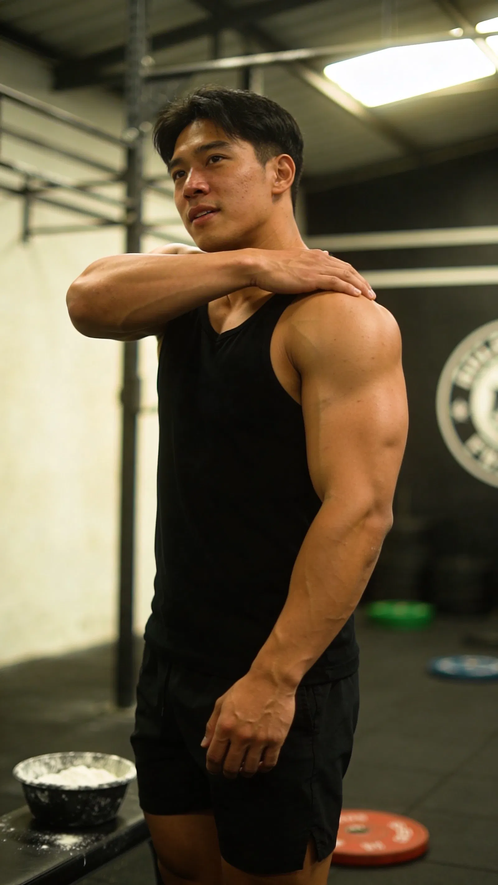 Southeast Asian male bodybuilder half-body gym portrait stretching shoulders with focused expression