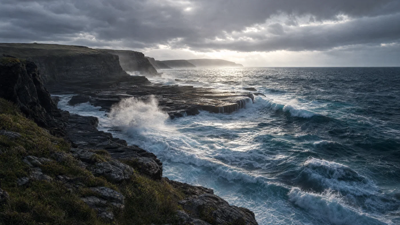 Stormy coastal cliffs with backlit sea spray, dark rocks, and cool blue-gray tones.