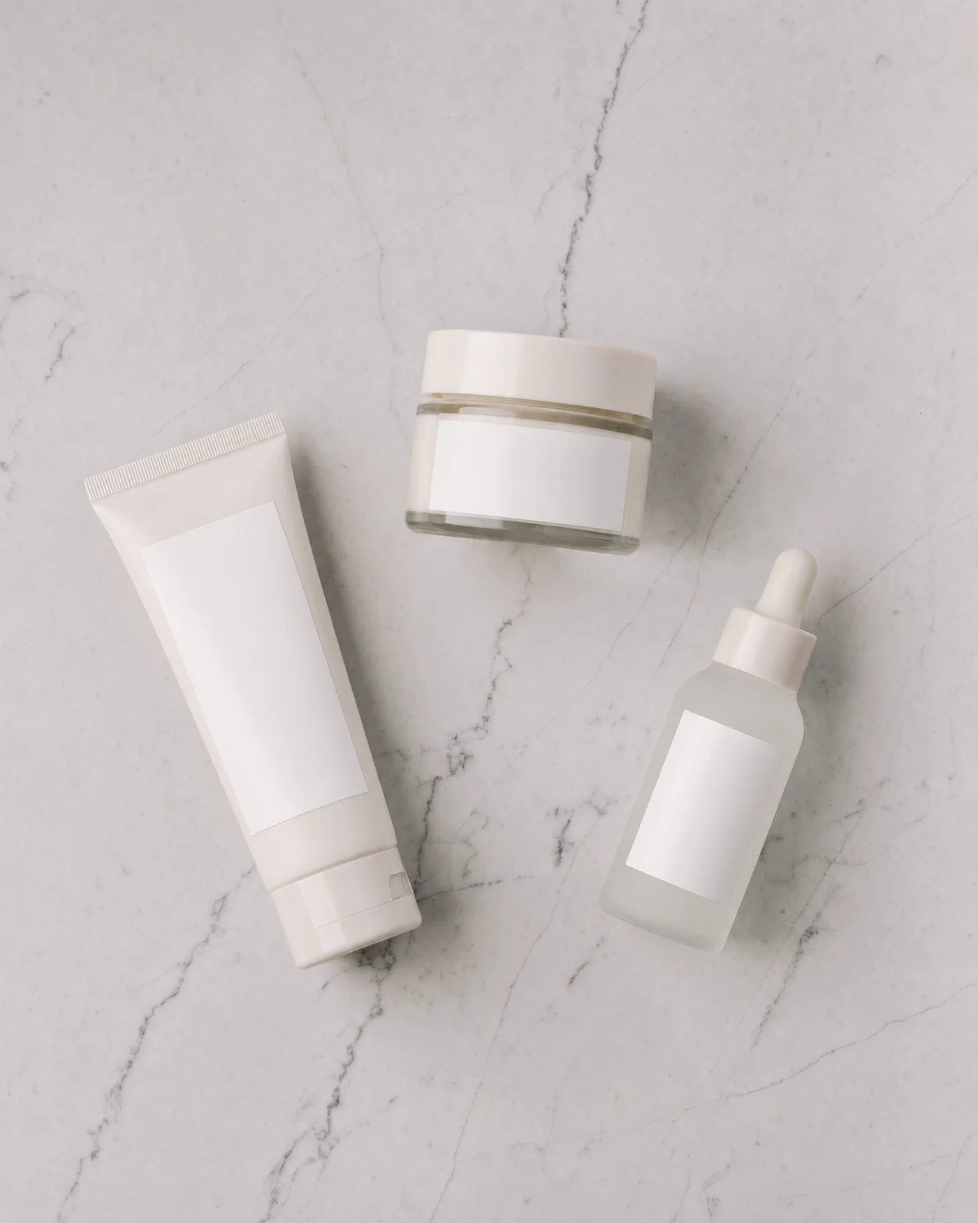 Top-down flat lay of skincare products on light gray marble with even overhead softbox lighting.
