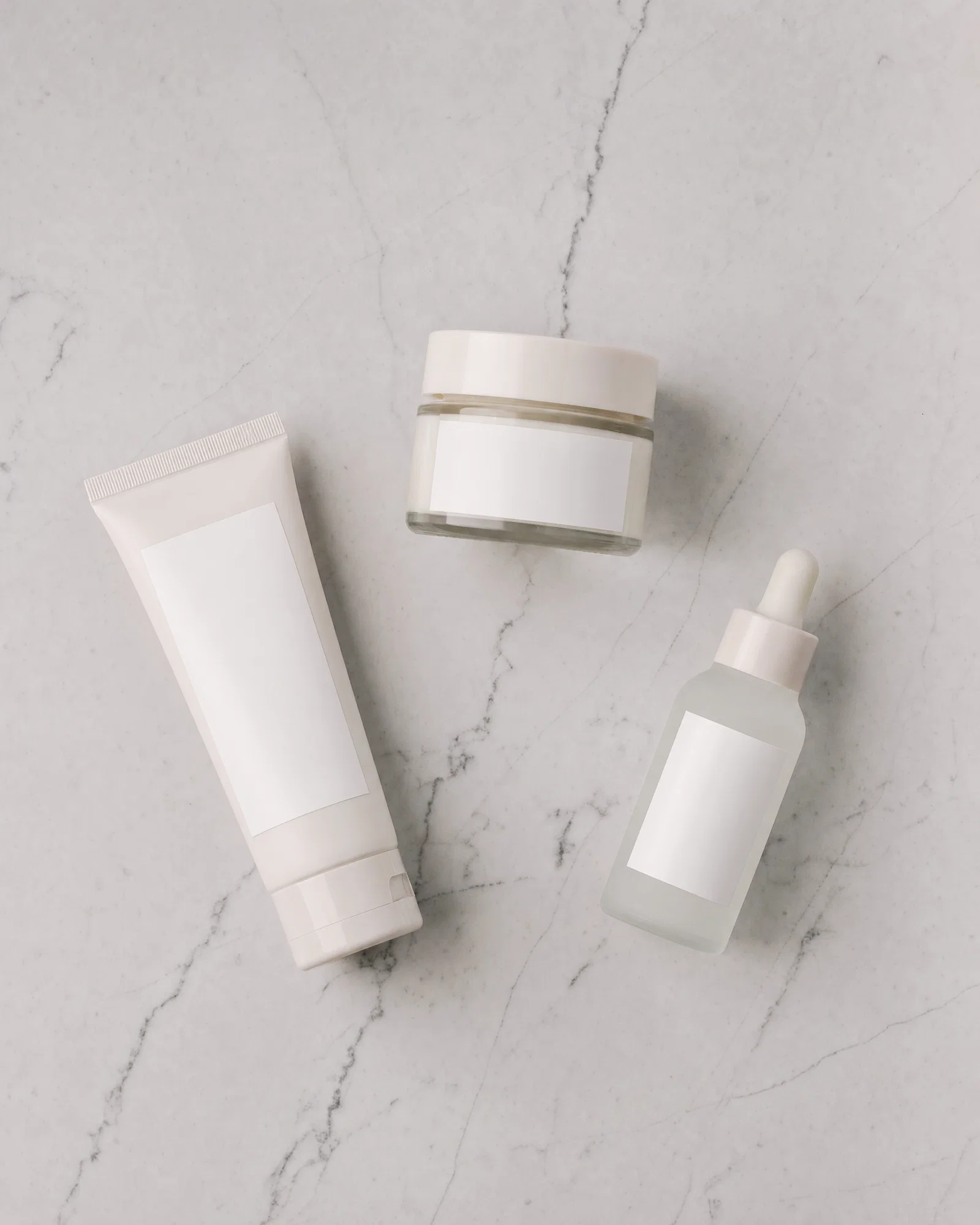 Top-down flat lay of skincare products on light gray marble with even overhead softbox lighting.