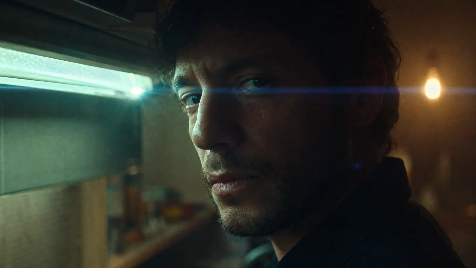 Widescreen extreme close-up with fluorescent practical key and strong horizontal anamorphic flare.