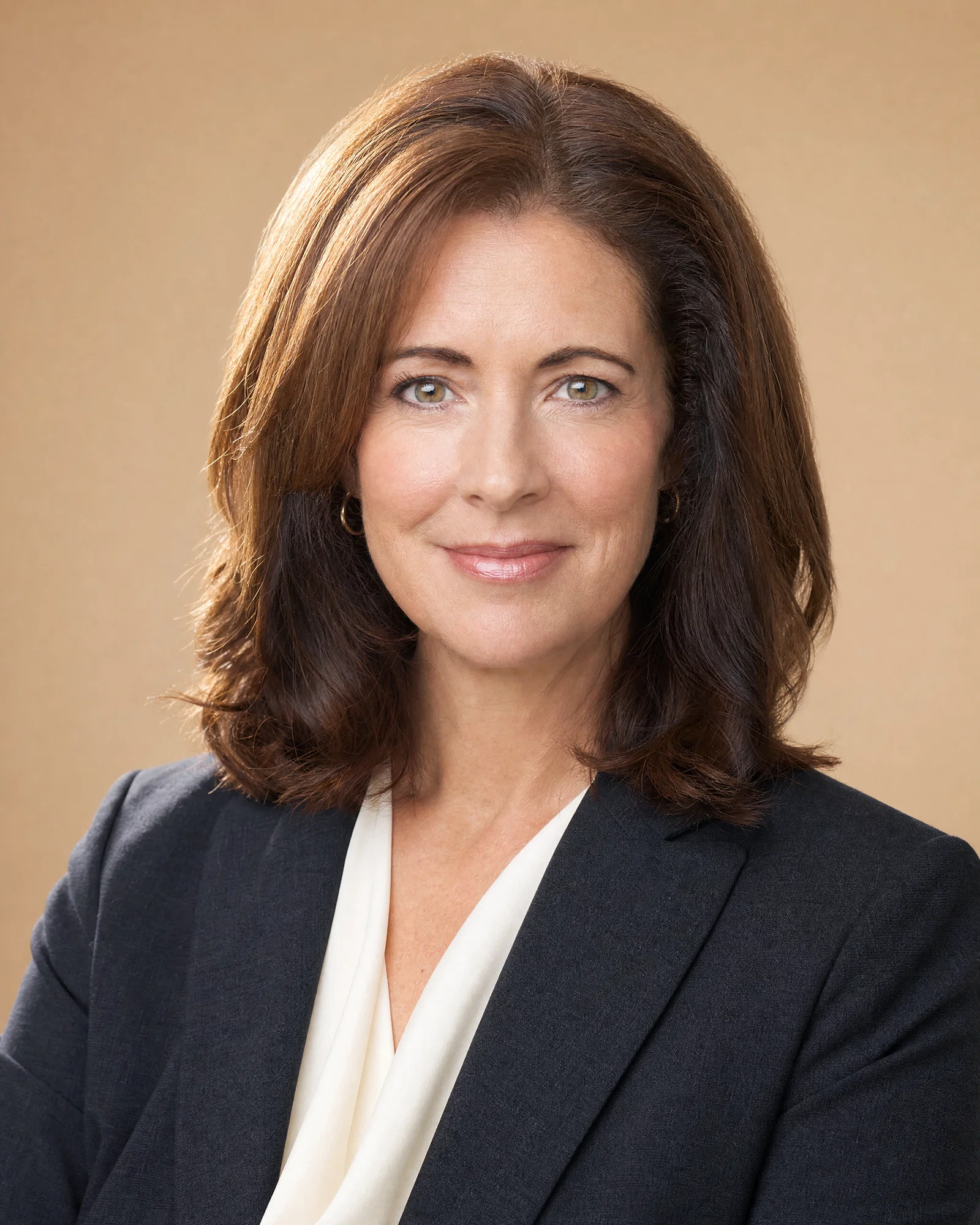 Woman in charcoal blazer on warm beige background with soft key and rim light.